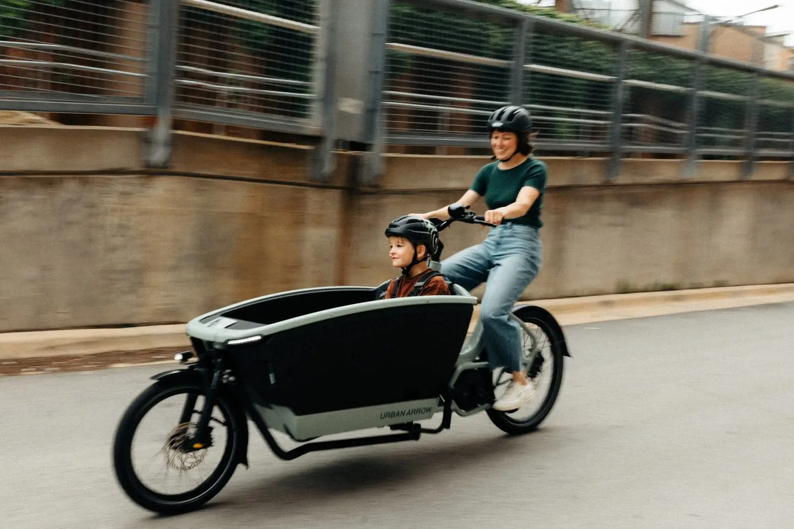 A parent riding an Urban Arrow Family cargo bike with a young child seated in the front box